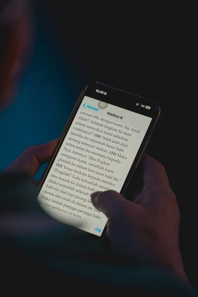 Close-up of hands holding a smartphone while reading a news article at night in Jakarta, Indonesia.